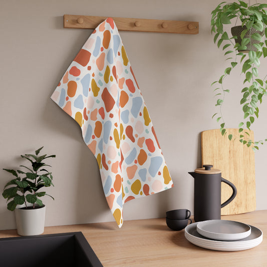 Colorful patterned towel hanging on a wooden rack in a kitchen setting with plants and utensils.